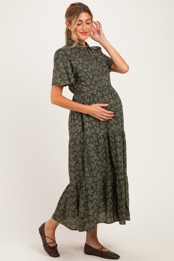 woman wearing a green floral maternity dress with a tiered skirt, gently cradling her baby bump