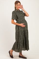 woman wearing a green floral maternity dress with a tiered skirt, gently cradling her baby bump