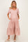 woman wearing a light pink maternity dress with a v-neck, short sleeves, and tiered skirt, holding her baby bump