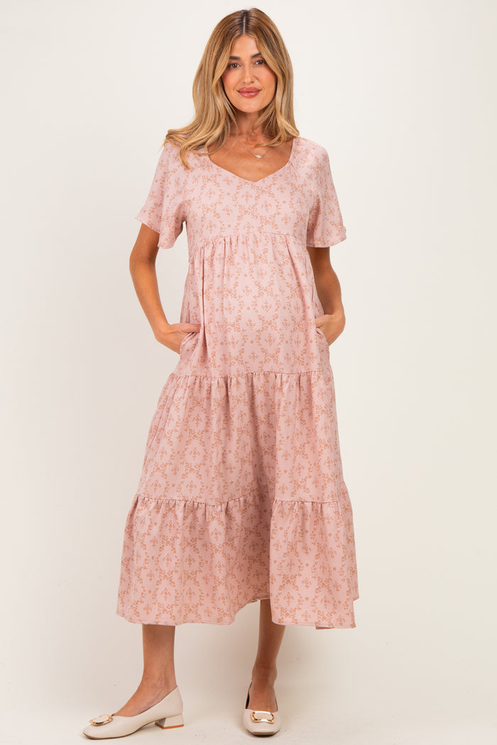 woman wearing a light pink maternity dress with a v-neck, short sleeves, and tiered skirt, holding her baby bump