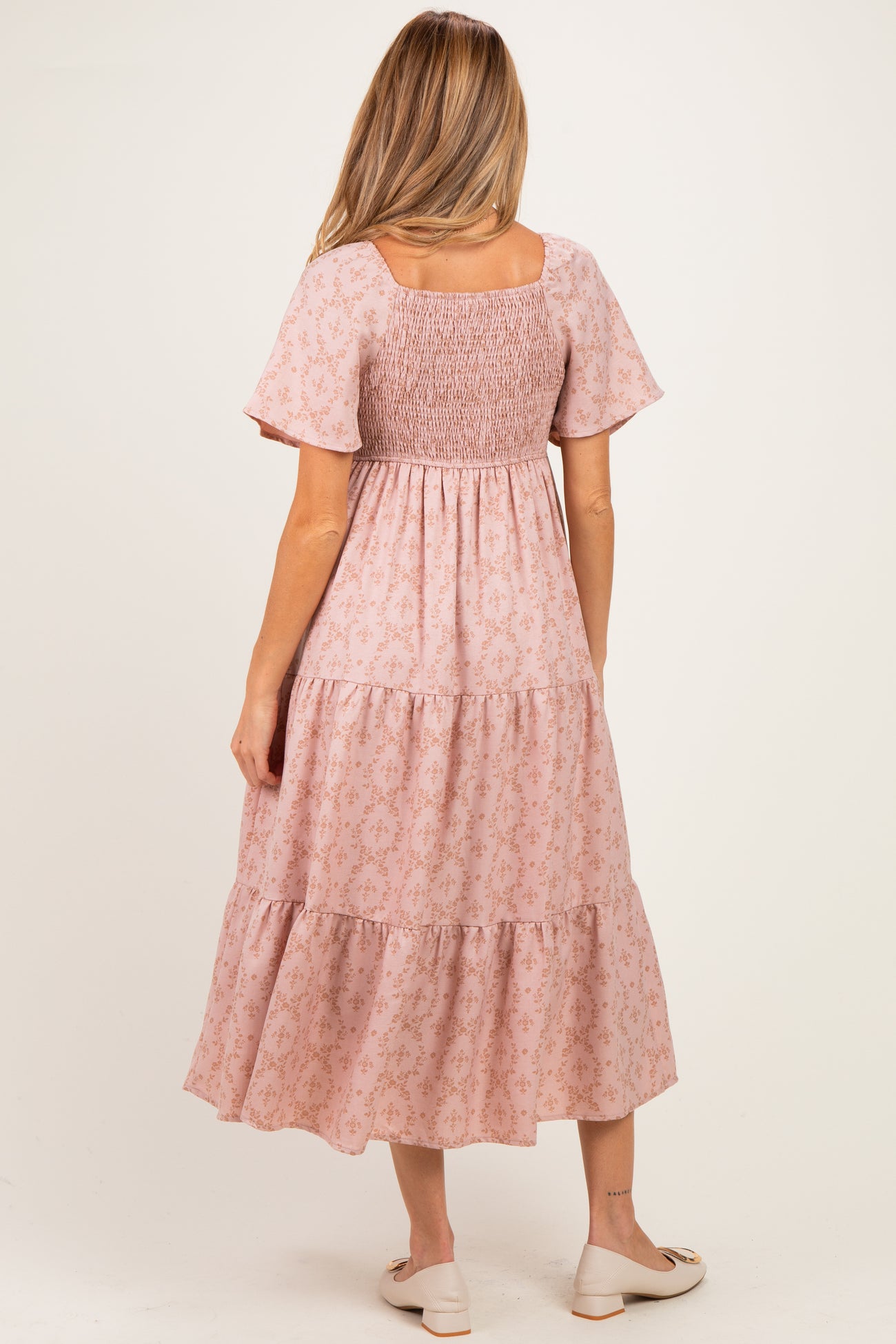 woman wearing a pink floral maternity dress with short sleeves and a smocked bodice, showing a baby bump