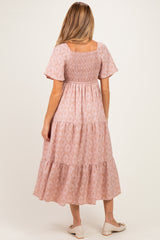 woman wearing a pink floral maternity dress with short sleeves and a smocked bodice, showing a baby bump