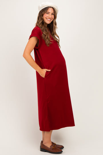 woman wearing a burgundy maternity dress with short sleeves and pockets, showing a baby bump