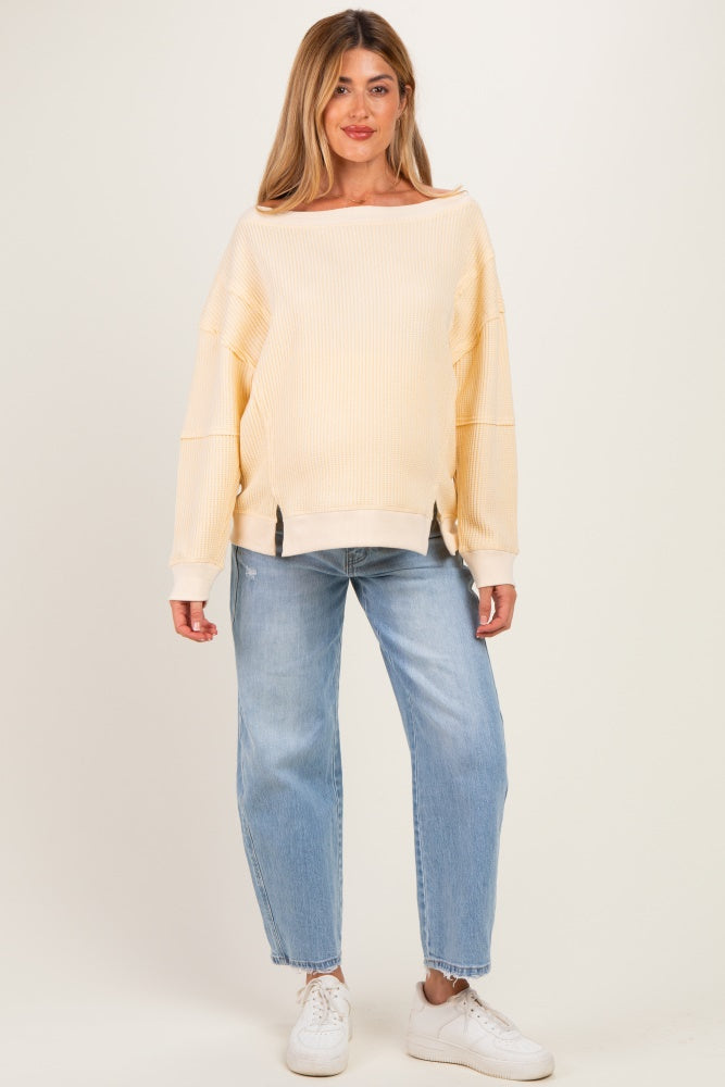 woman wearing a light yellow ribbed maternity sweatshirt with a relaxed fit and paired with light blue jeans