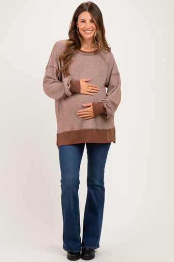 woman wearing a brown maternity sweater with ribbed texture and flared jeans, holding her baby bump