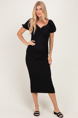 woman wearing a black midi dress with puff sleeves and ruched detailing, standing with one hand on her hip