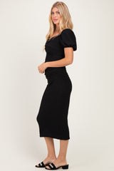 woman wearing a black puff sleeve midi dress with ruched detailing and open-toe slide sandals