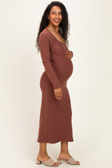 woman wearing a rust long sleeve maternity dress, showing off her baby bump, smiling while standing sideways