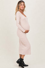 woman wearing a light beige long sleeve maternity dress and holding her baby bump
