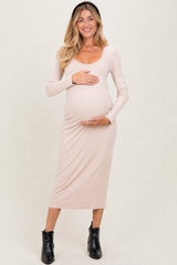 woman wearing a beige long sleeve maternity dress and holding her baby bump