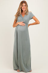 woman wearing a sage green short sleeve maternity maxi dress and holding her baby bump