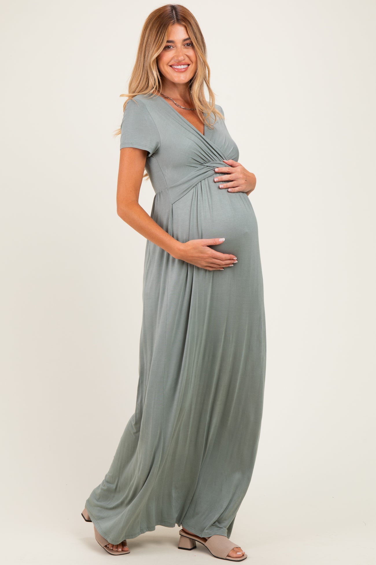 woman wearing a green short sleeve maternity maxi dress and holding her baby bump