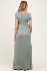 woman wearing a sage green short sleeve maternity maxi dress, showing a flowing silhouette from the back
