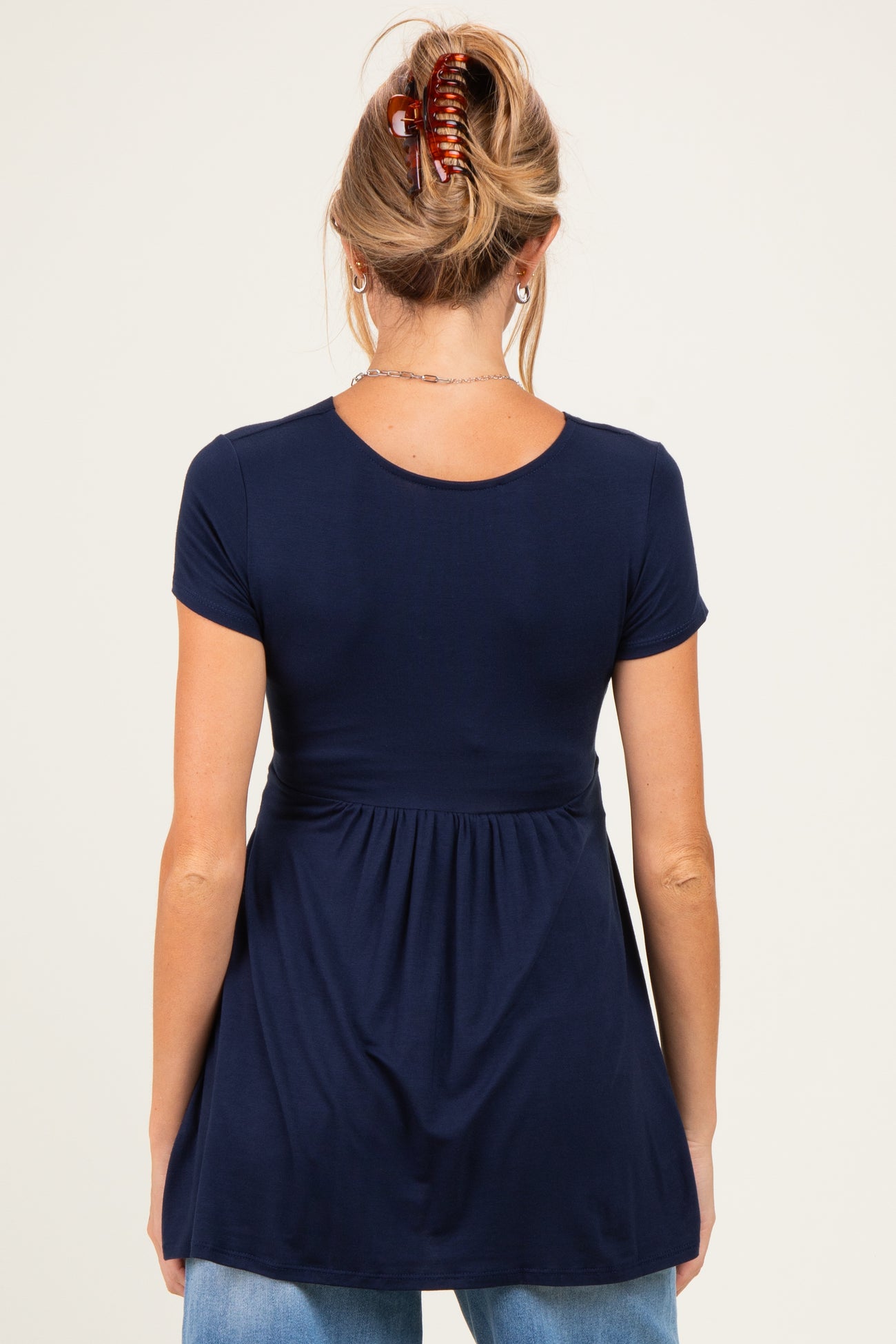woman wearing a navy blue maternity top with short sleeves and a fitted bodice that flares at the waist