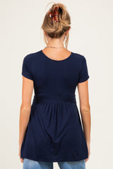 woman wearing a navy blue maternity top with short sleeves and a fitted bodice that flares at the waist
