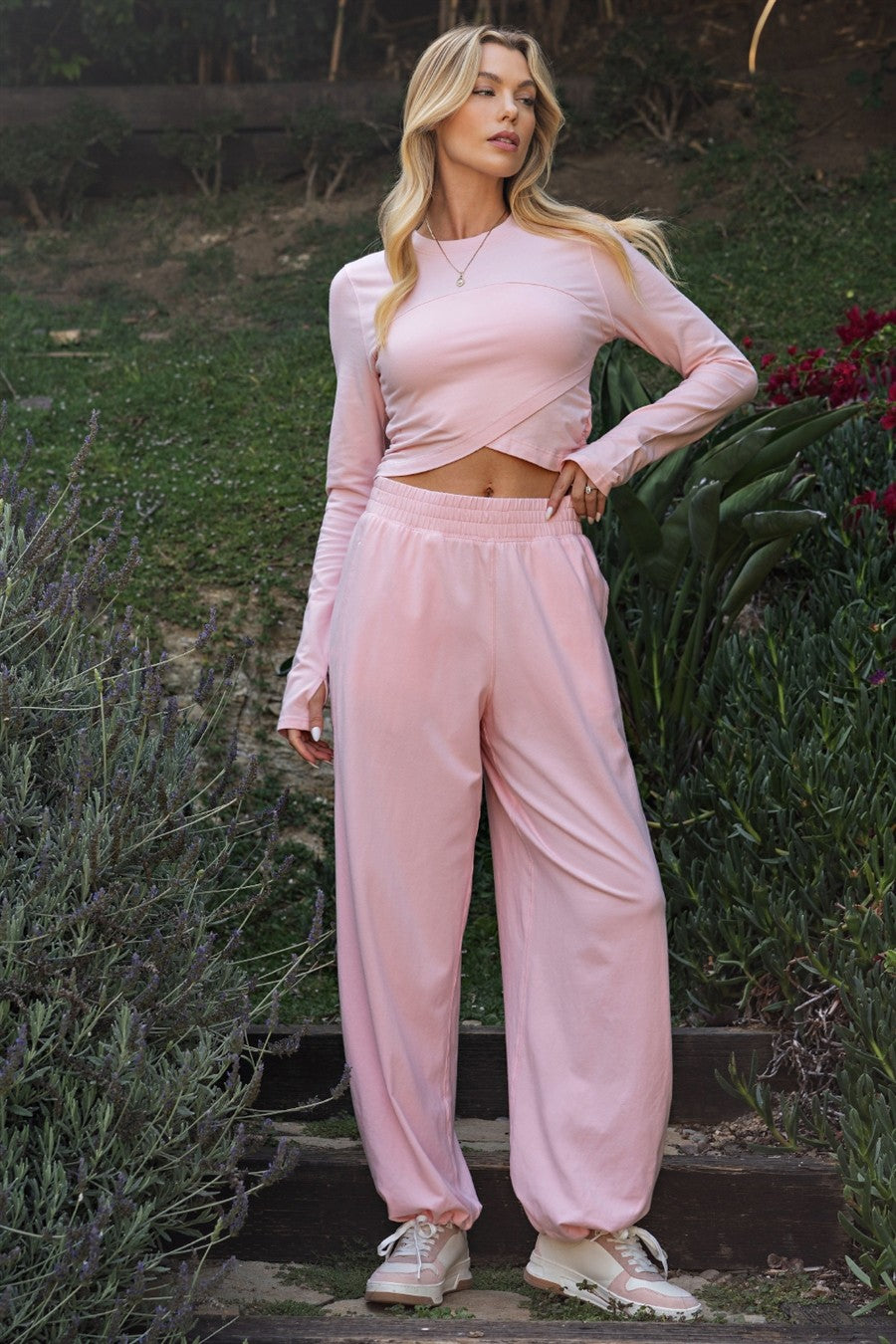 woman wearing a light pink long sleeve cropped top with matching blush joggers and sneakers, standing outdoors