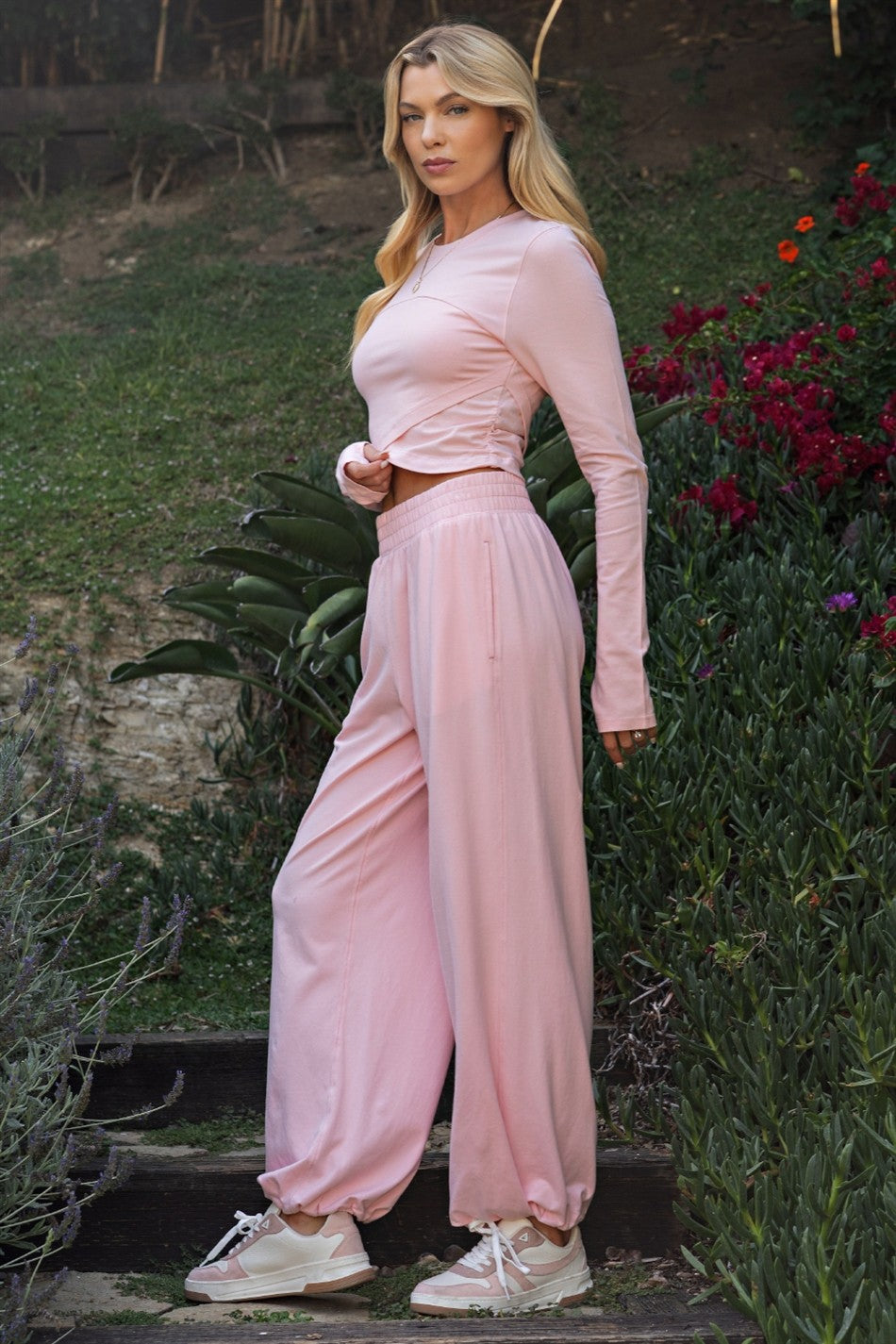woman wearing a light pink long sleeve top with gathered detail and matching loose-fit pants in a garden setting