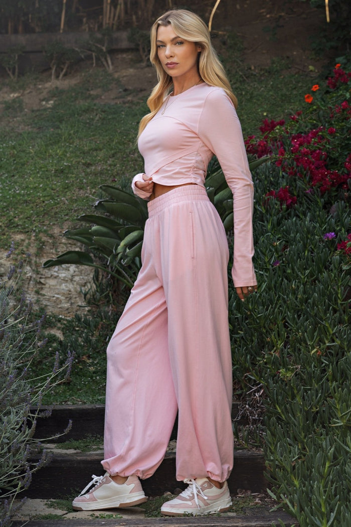 woman wearing a light pink long sleeve top with gathered detail and matching loose-fit pants in a garden setting