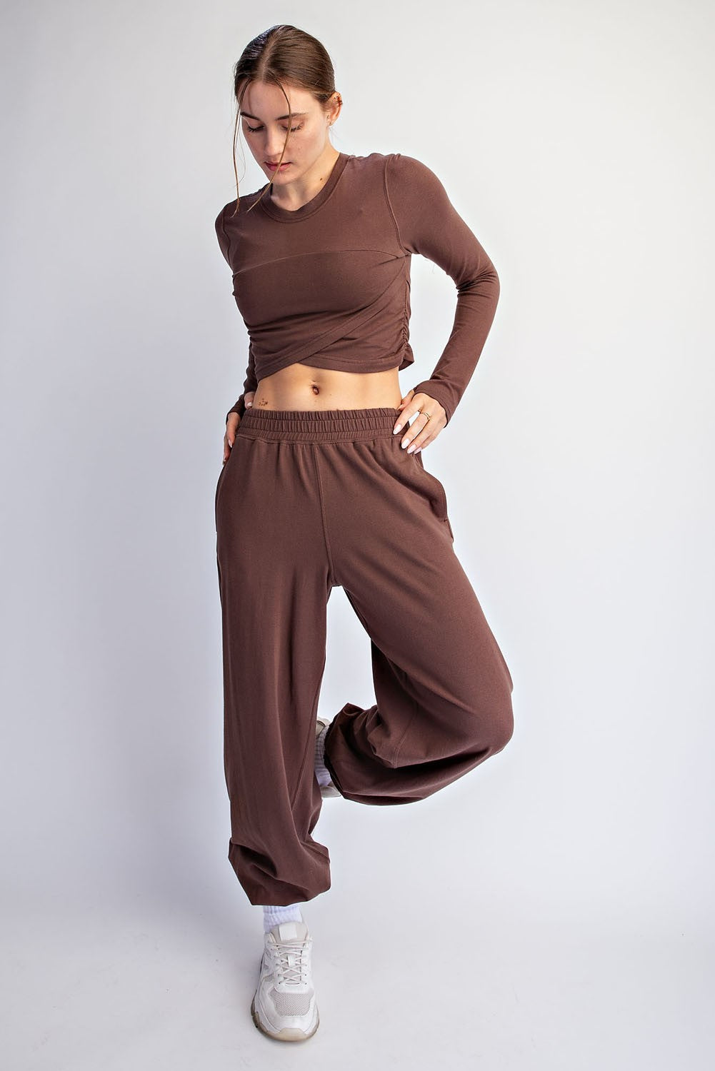 woman wearing a brown long sleeve cropped top and matching wide-leg pants, styled with white sneakers