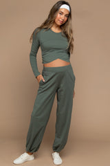 woman wearing a green maternity long sleeve top with a twist front and matching jogger pants, showing her baby bump