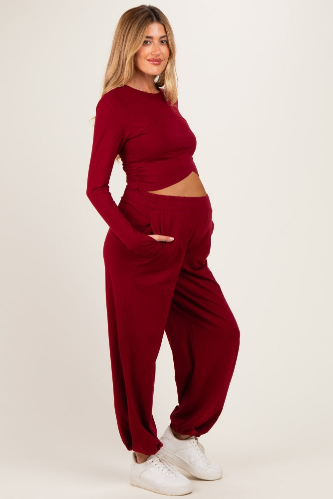 woman wearing a burgundy long sleeve maternity top and matching jogger pants, revealing baby bump with a relaxed fit