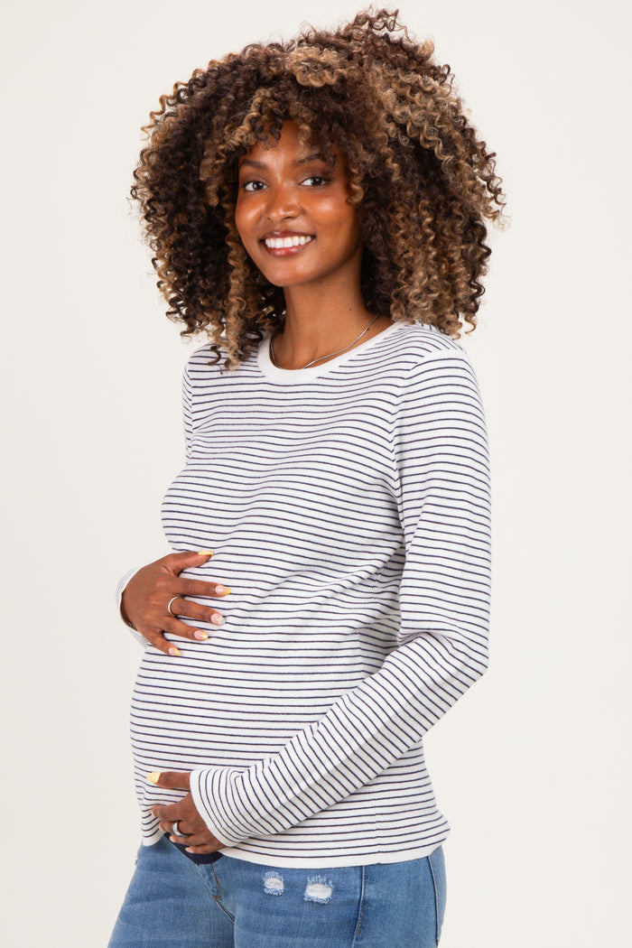 woman wearing a gray and white striped maternity top and holding her baby bump with a smile