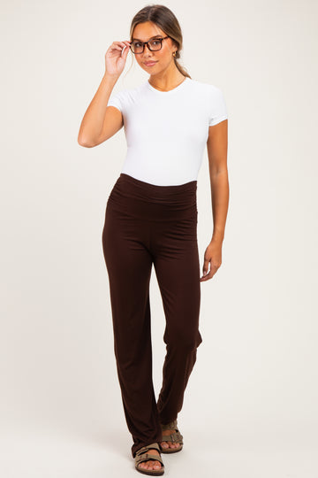 woman wearing a white short sleeve maternity top and brown maternity pants, styled with glasses and a relaxed pose