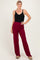 woman wearing a black ribbed sleeveless top and burgundy wide-leg pants, smiling and posing with one hand on her hip