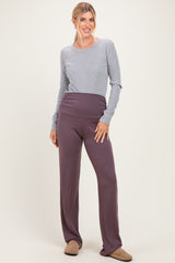 woman wearing a gray long sleeve top and purple high-waisted pants, posing against a light background