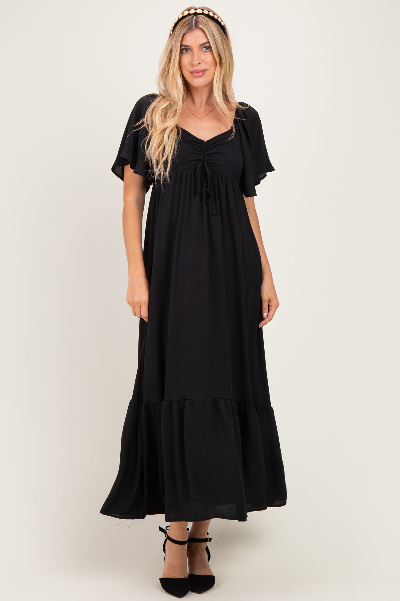 woman wearing a black maxi dress with short flutter sleeves and a tie front detail