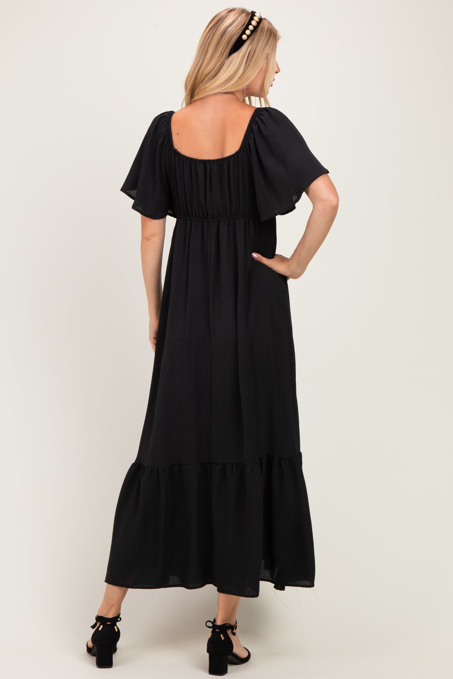 woman wearing a black maxi dress with tiered hem and short flutter sleeves, viewed from the back