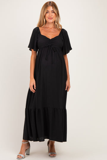 woman wearing a black maternity maxi dress with short flutter sleeves and a ruffled hem, showcasing her baby bump