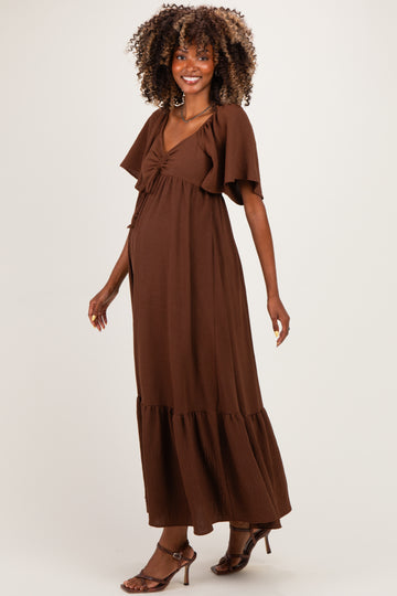 woman wearing a brown maternity maxi dress with flutter sleeves and a gathered waist, showcasing her baby bump