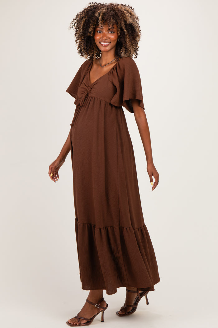 woman wearing a brown maternity maxi dress with flutter sleeves and a gathered waist, showcasing her baby bump