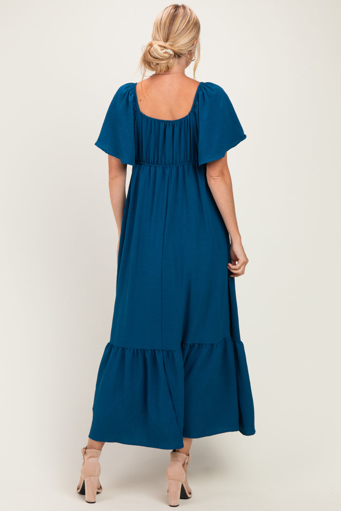 woman wearing a teal off-the-shoulder maxi dress with flutter sleeves and a tiered skirt, seen from the back