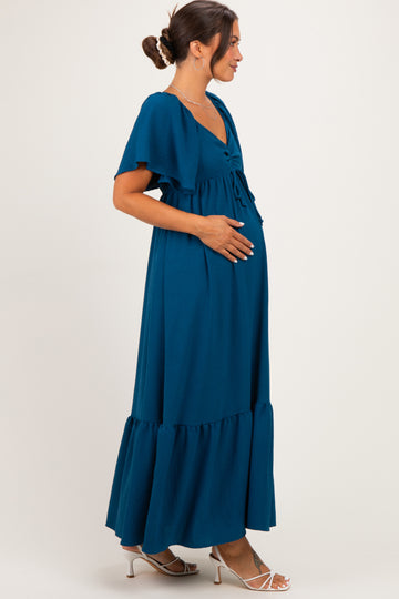woman wearing a teal maternity maxi dress with flutter sleeves and a baby bump visible