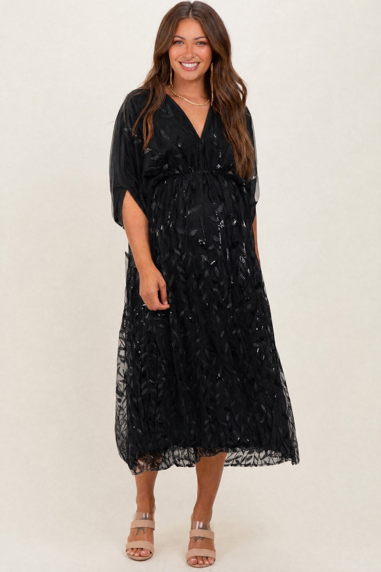 woman wearing a black maternity dress with a flowy silhouette and sequin detailing, showing her baby bump