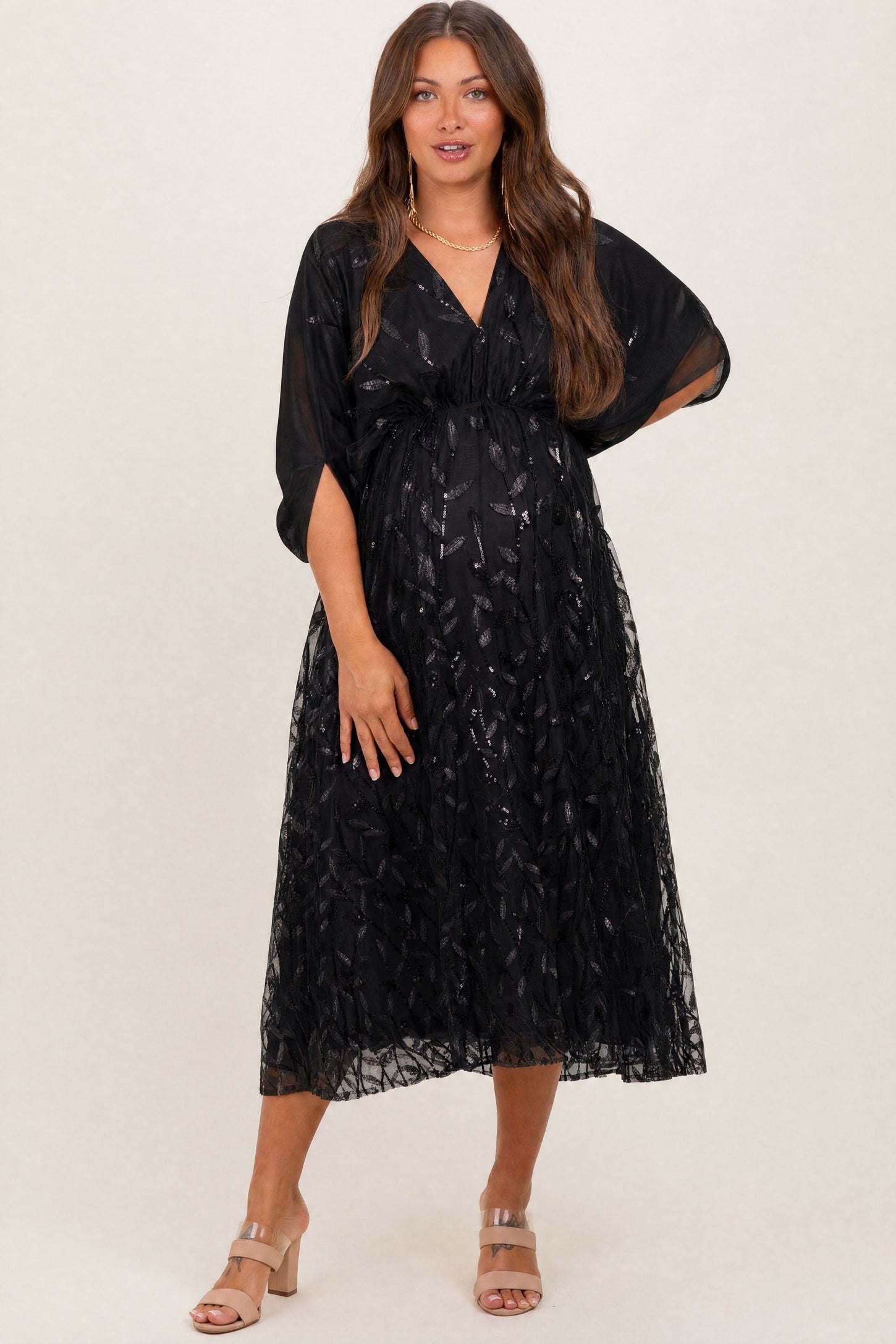 woman wearing a black maternity dress with sheer overlay and short sleeves, displaying her baby bump
