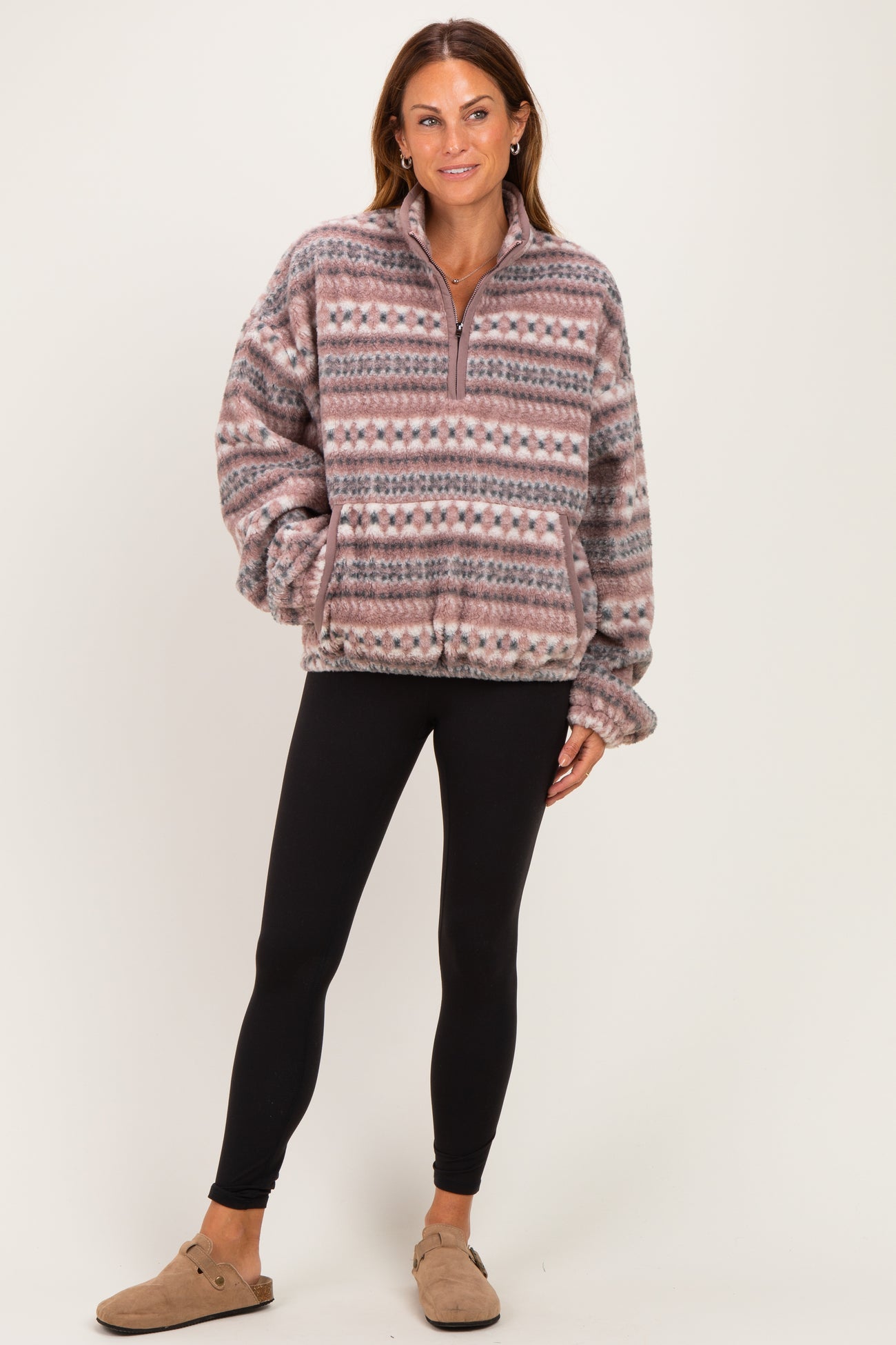 woman wearing a cozy patterned fleece pullover in pink and gray with black leggings and tan slip-on shoes
