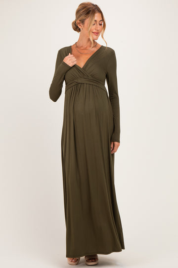 woman wearing an olive green long sleeve maternity dress with a fitted bodice and flowing skirt, showing her baby bump