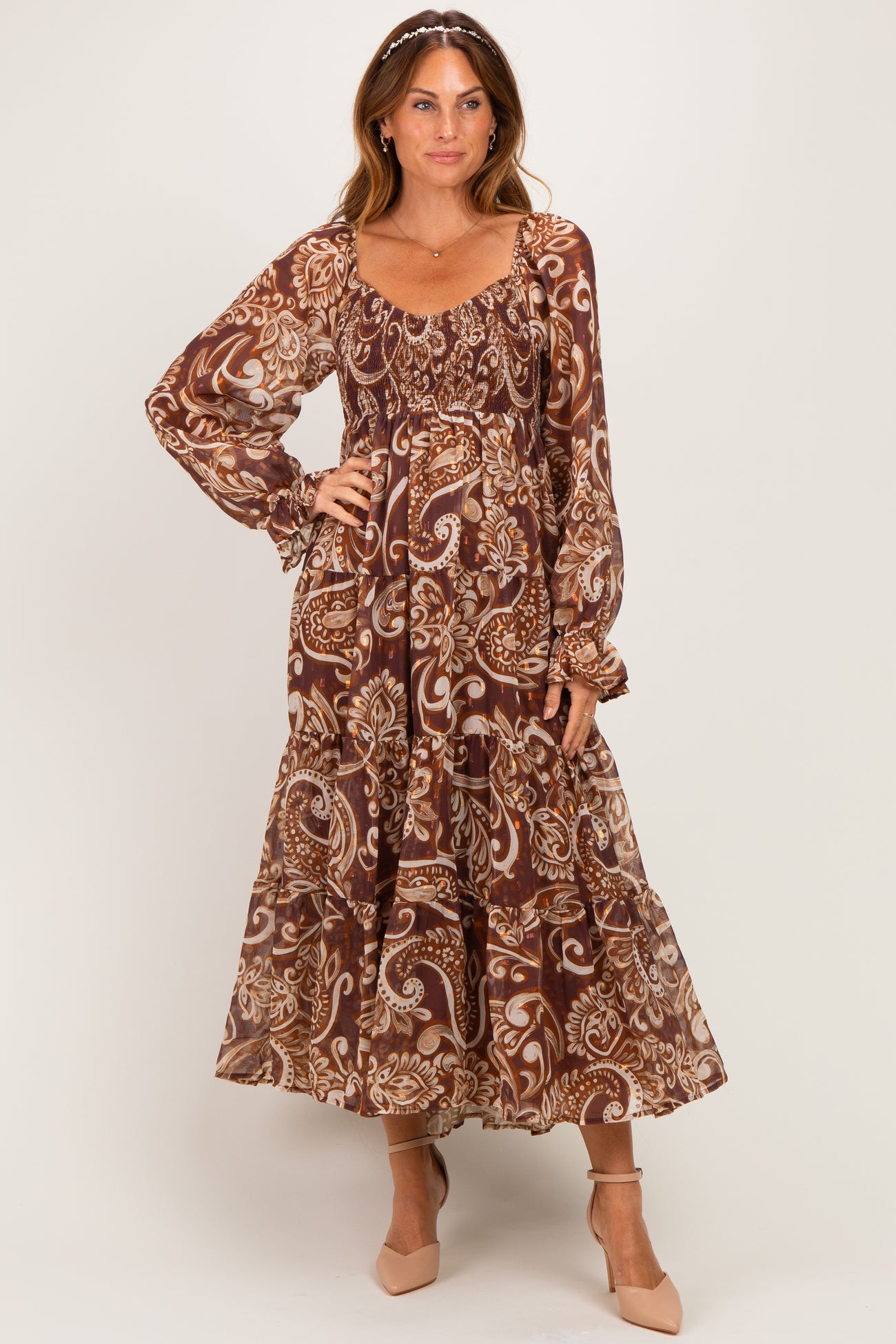 woman wearing a long brown paisley print maxi dress with puff sleeves and a tiered skirt