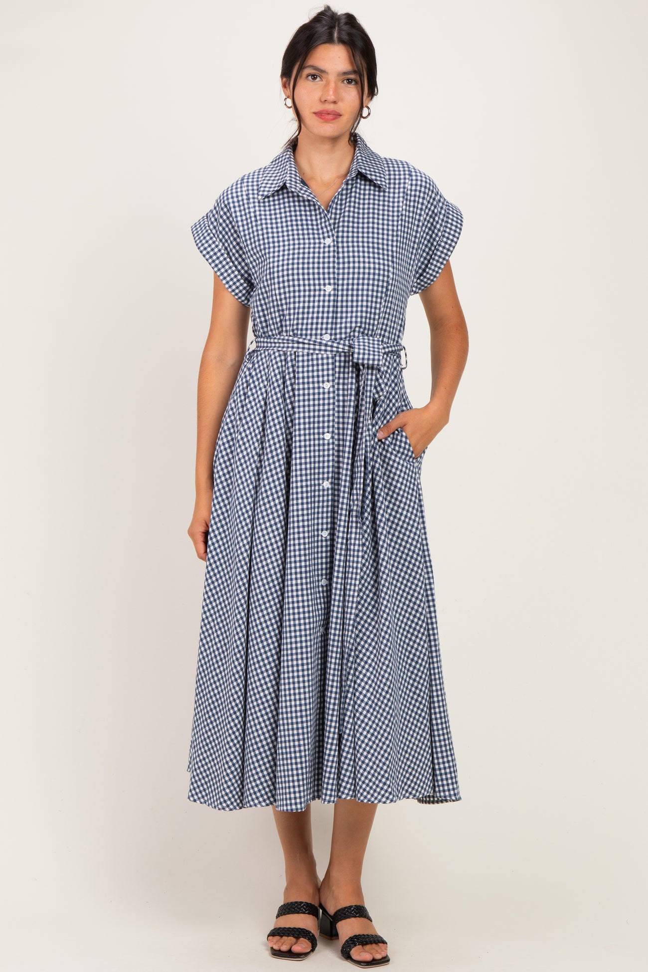 woman wearing a navy blue gingham midi dress with short sleeves and a tie belt, standing with hands in pockets