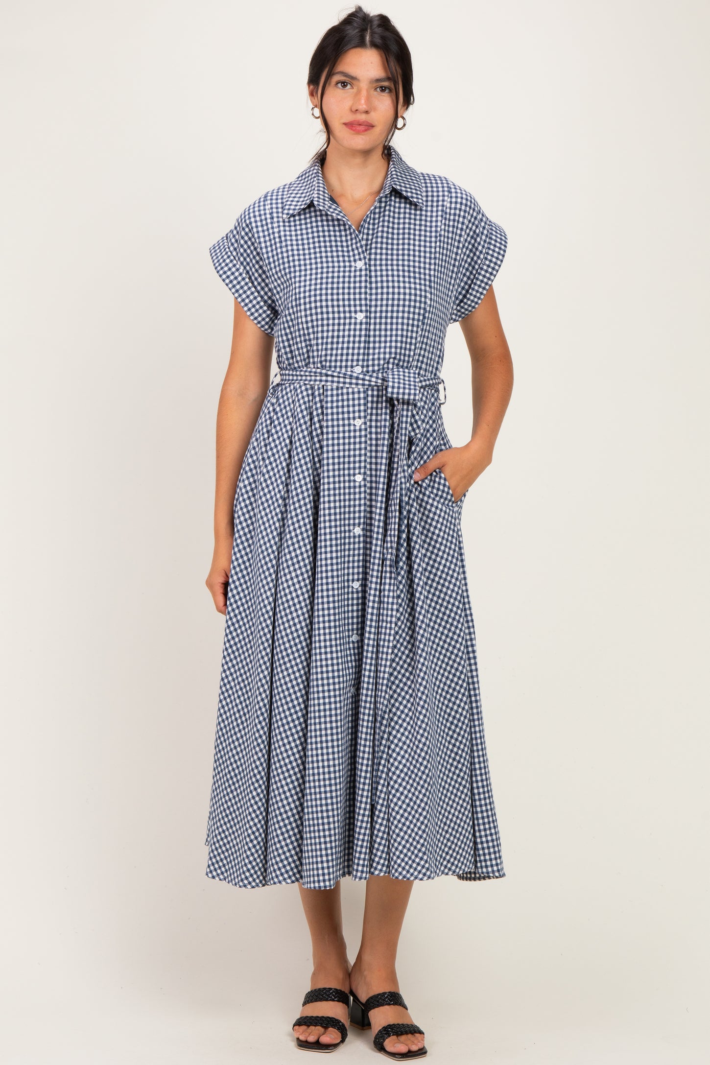 woman wearing a navy blue gingham midi dress with short sleeves and a tie belt, standing with hands in pockets