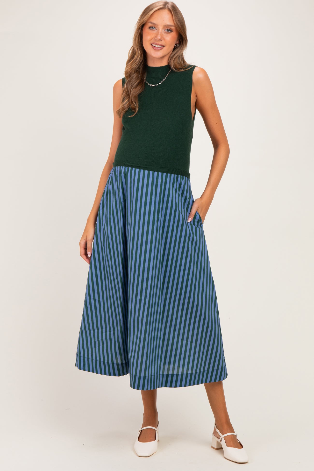 woman wearing a green sleeveless top and a blue and green striped maternity skirt with pockets, showing her baby bump