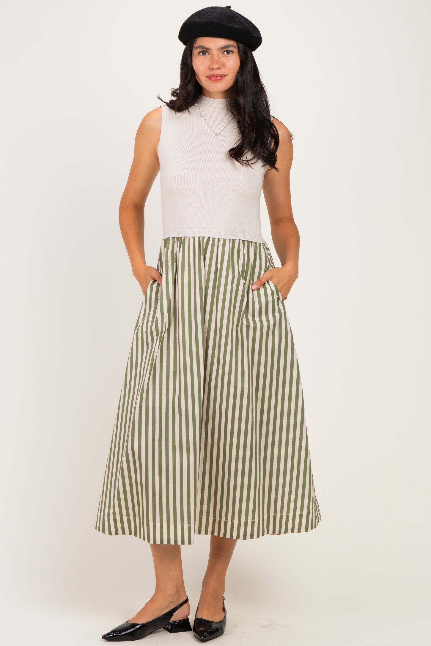 woman wearing a sleeveless cream top and a green and white striped midi skirt with pockets