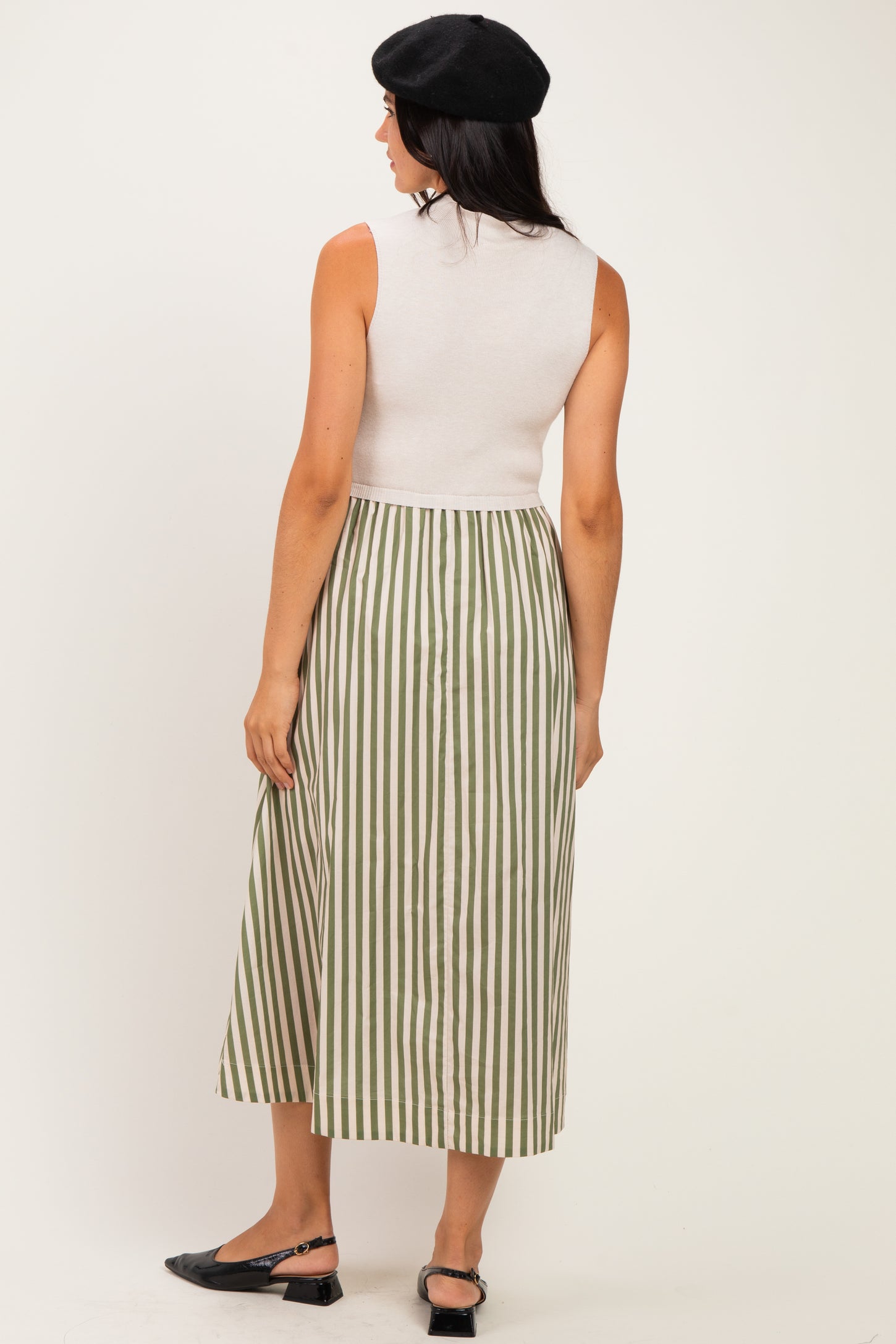 woman wearing a sleeveless white top and a long green and white striped skirt, viewed from the back