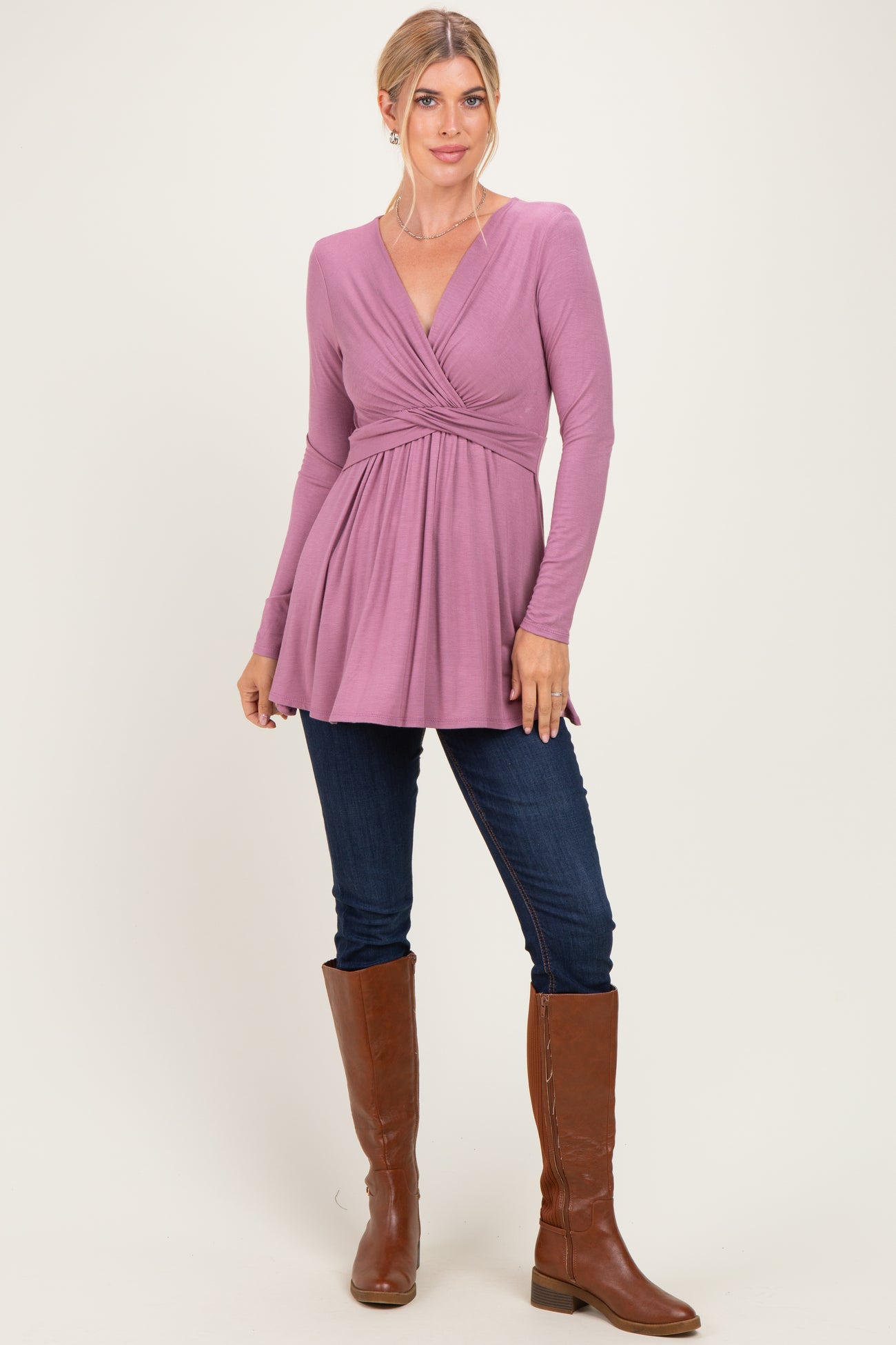 woman wearing a dusty rose long sleeve wrap top with a gathered waist, paired with skinny jeans and tall brown boots