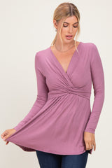 woman wearing a mauve long sleeve wrap top with a twisted front detail and flared hemline paired with dark jeans