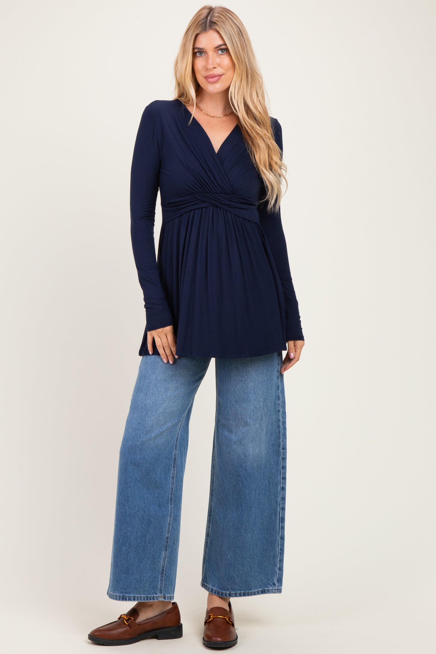woman wearing a navy long sleeve wrap top with a gathered bodice and blue wide-leg jeans