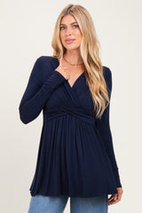 woman wearing a navy long sleeve wrap top with a gathered front and flared hem, paired with light blue jeans